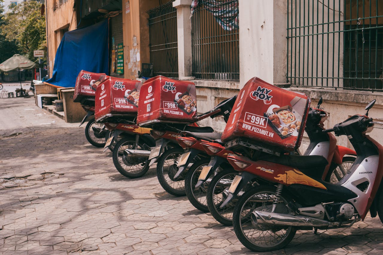 Motorbikes with branded delivery boxes parked on an urban sidewalk, showcasing food delivery services.